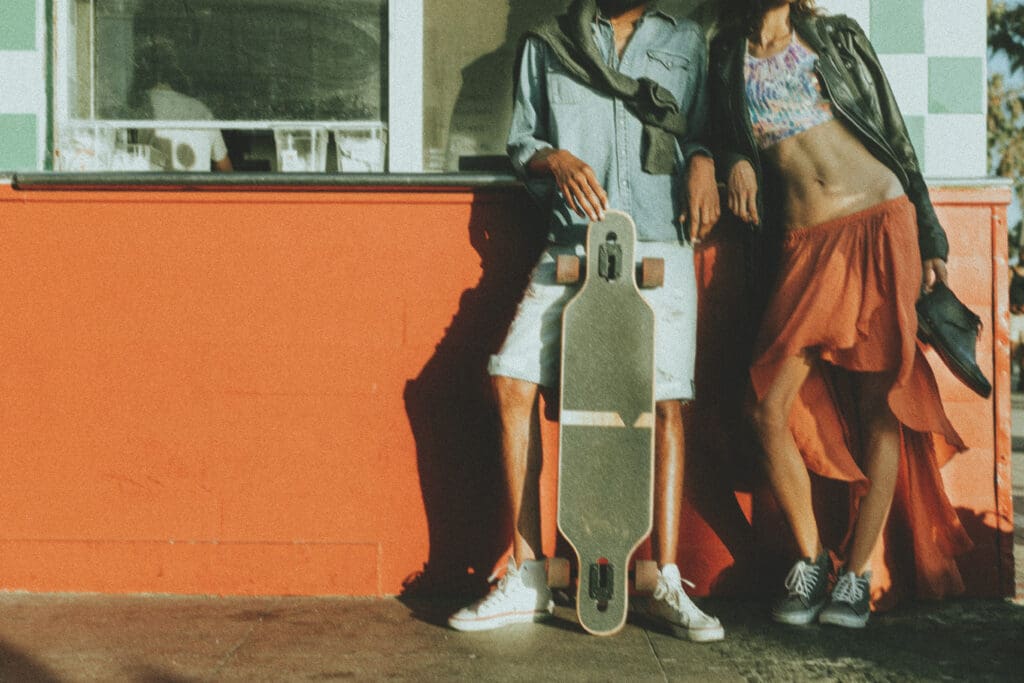Zen Den Co. HR retro logo on an orange storefront wall with a person holding a longboard skateboard in a vintage surf-inspired brand photo