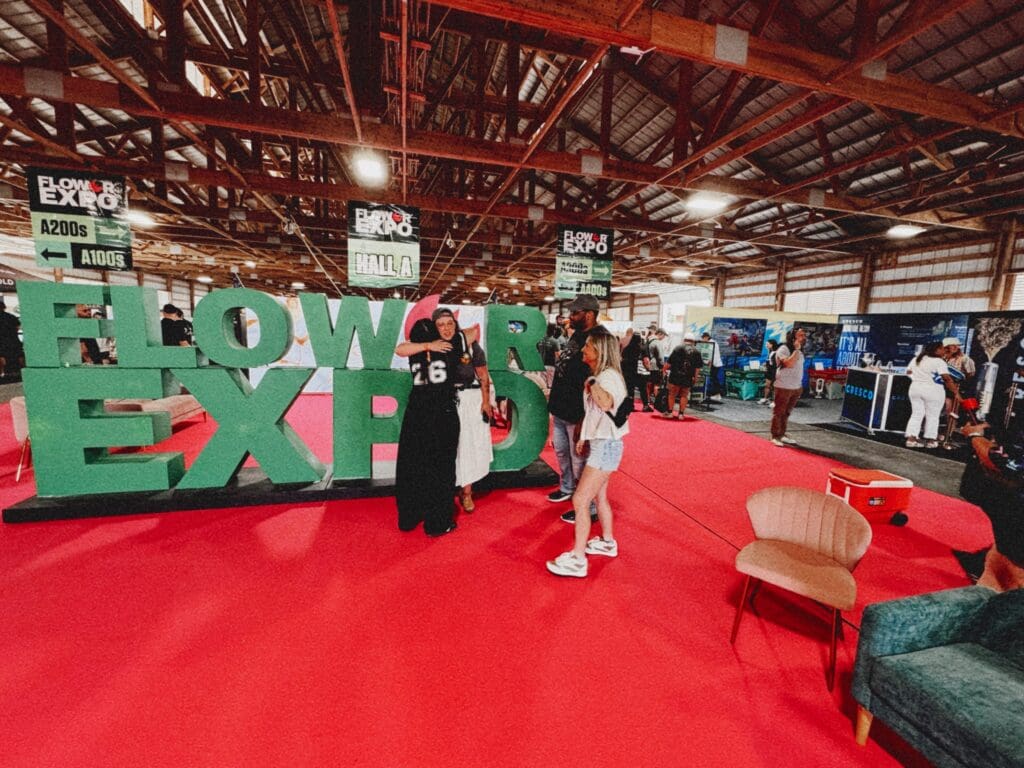 Four cannabis industry friends in front of the Flower Expo MA 2026 sign on the pink carpet in Hall A